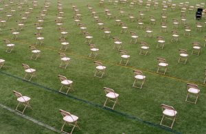 White folding chairs on a football field, placed in a socially distant pattern