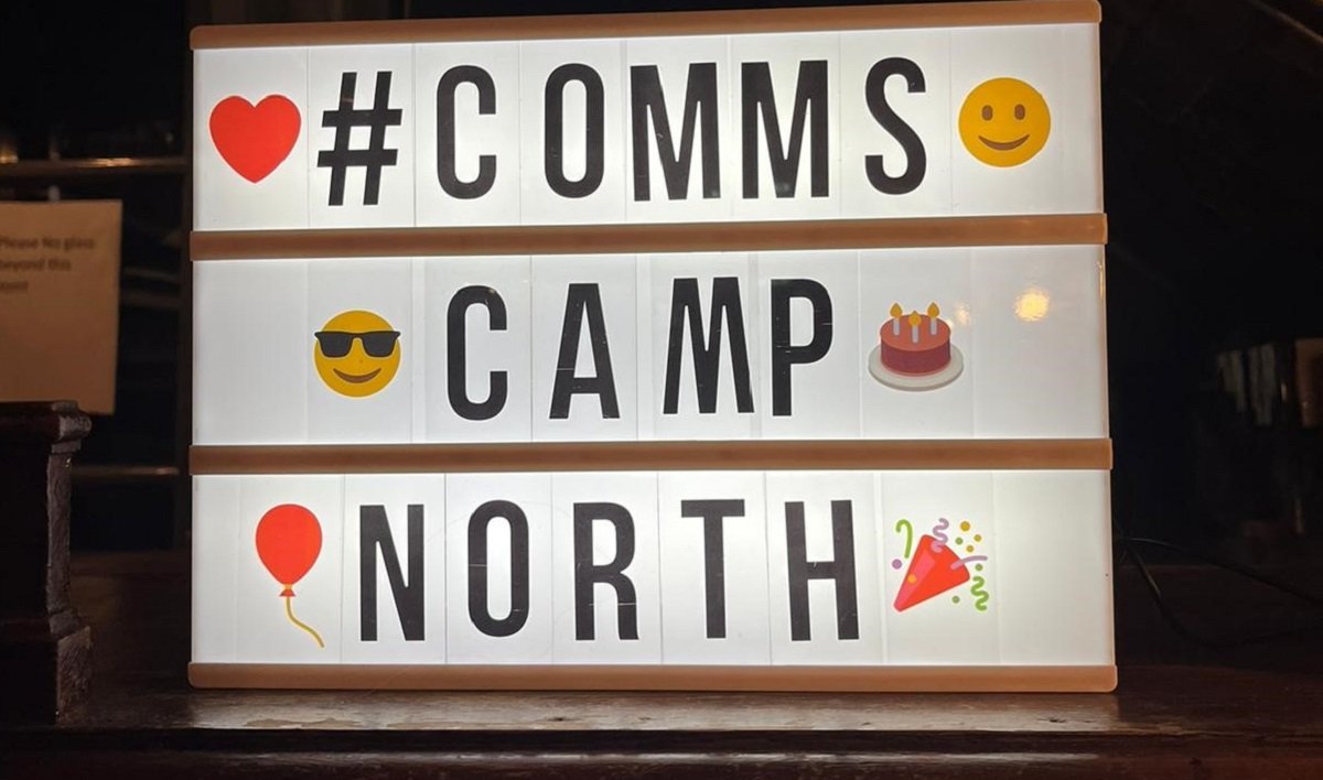 A back lit white sign with emojis and #CommsCampNorth written on it