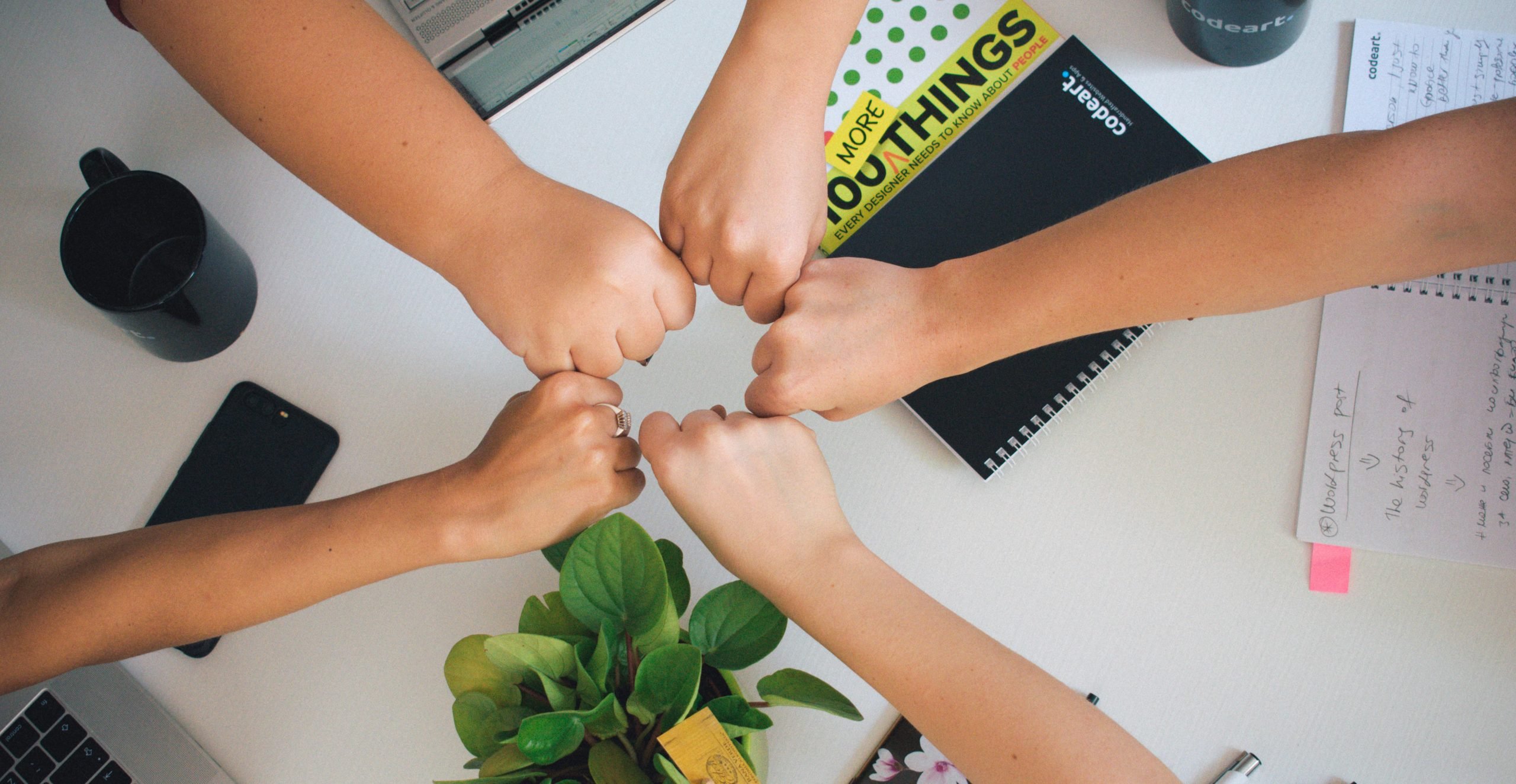 Five closed hands doing a group fist bump above a desk